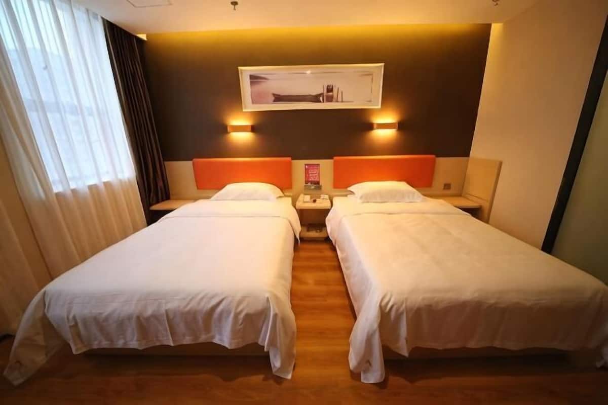 Una habitación de hotel con dos camas, una mesita de noche, una lámpara y un cuadro en la pared.