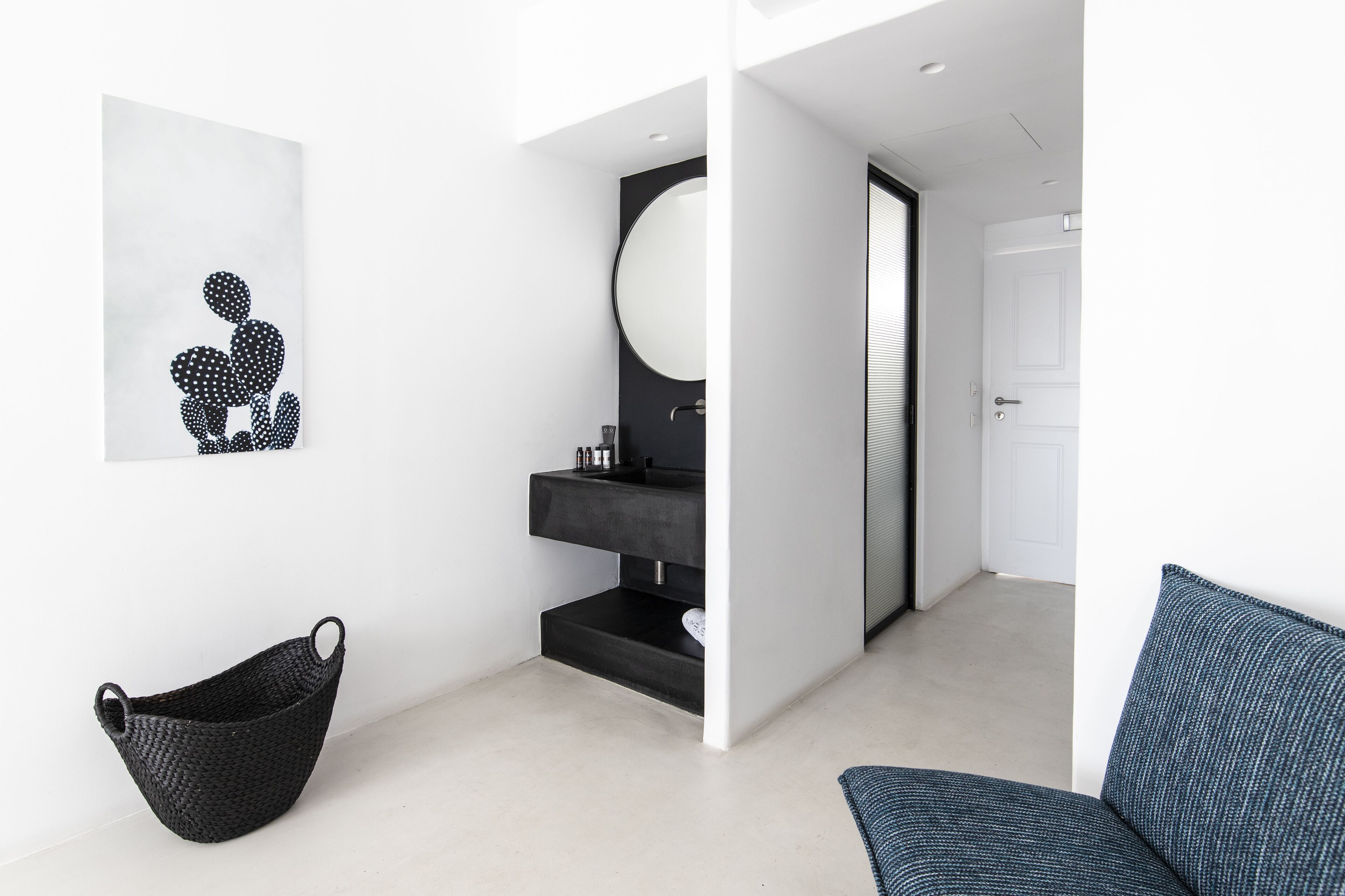 Un baño moderno con un lavamanos negro, un espejo redondo y una puerta blanca.