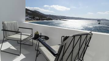 A balcony with two chairs and a small table, overlooking a coastal view with boats and buildings.