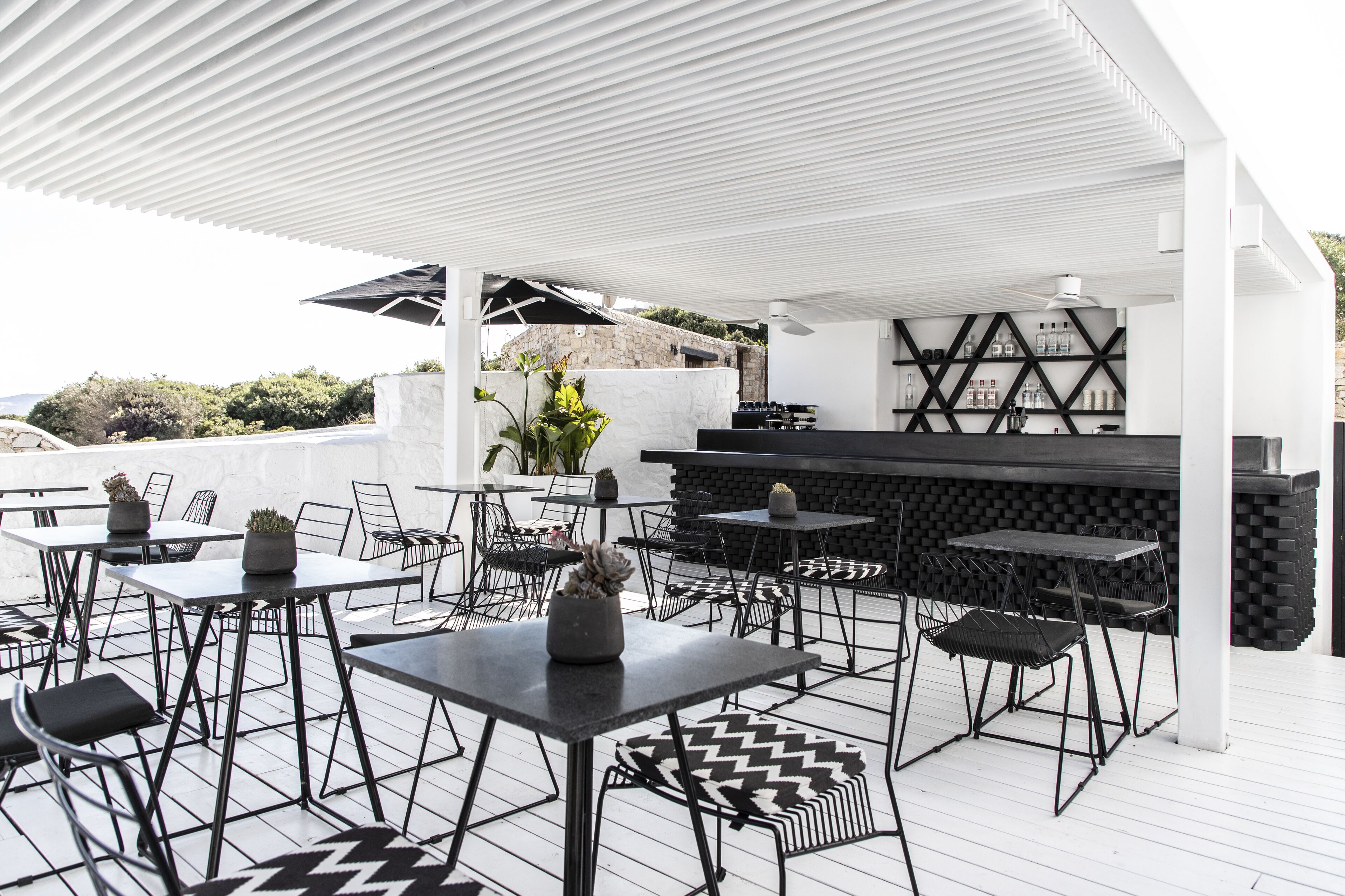 Eine Terrasse im Freien mit Tischen, Stühlen, einer Bar und einer Wand aus Stein.