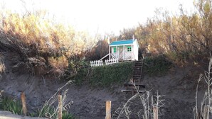 Ein kleines Haus mit blauem Dach und weißen Wänden, gelegen an einem sandigen Hang mit weißem Zaun.