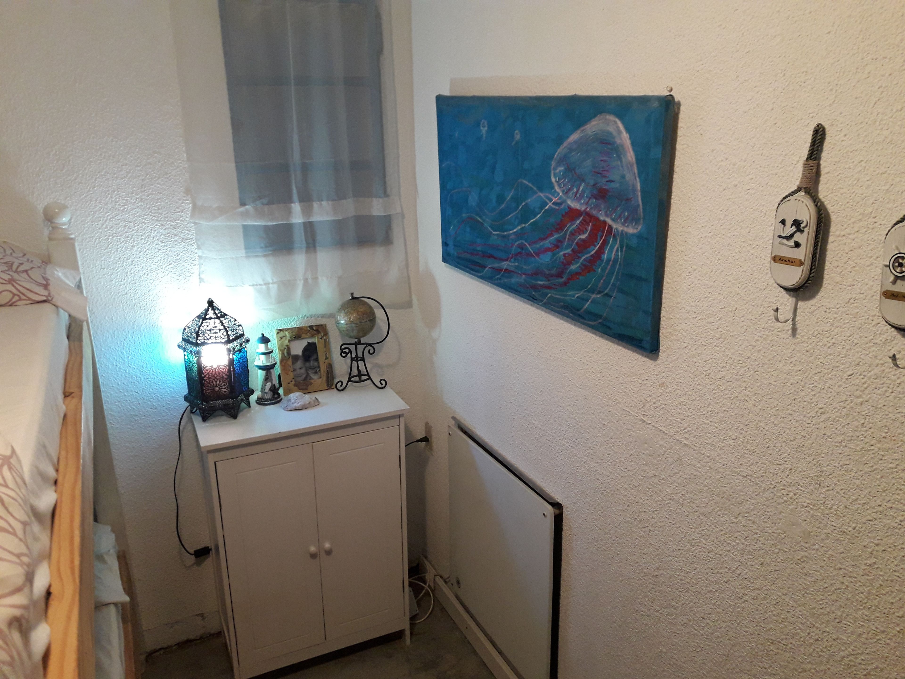 Ein Schlafzimmer mit einem Bett, einem Nachttisch mit Lampe, einem Globus und einem Bild von einer Qualle.