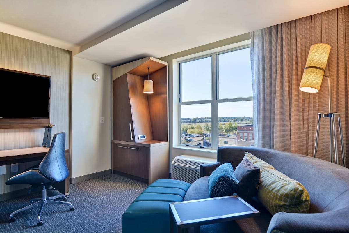 A hotel room with a desk, chair, and a large window offering a city view.