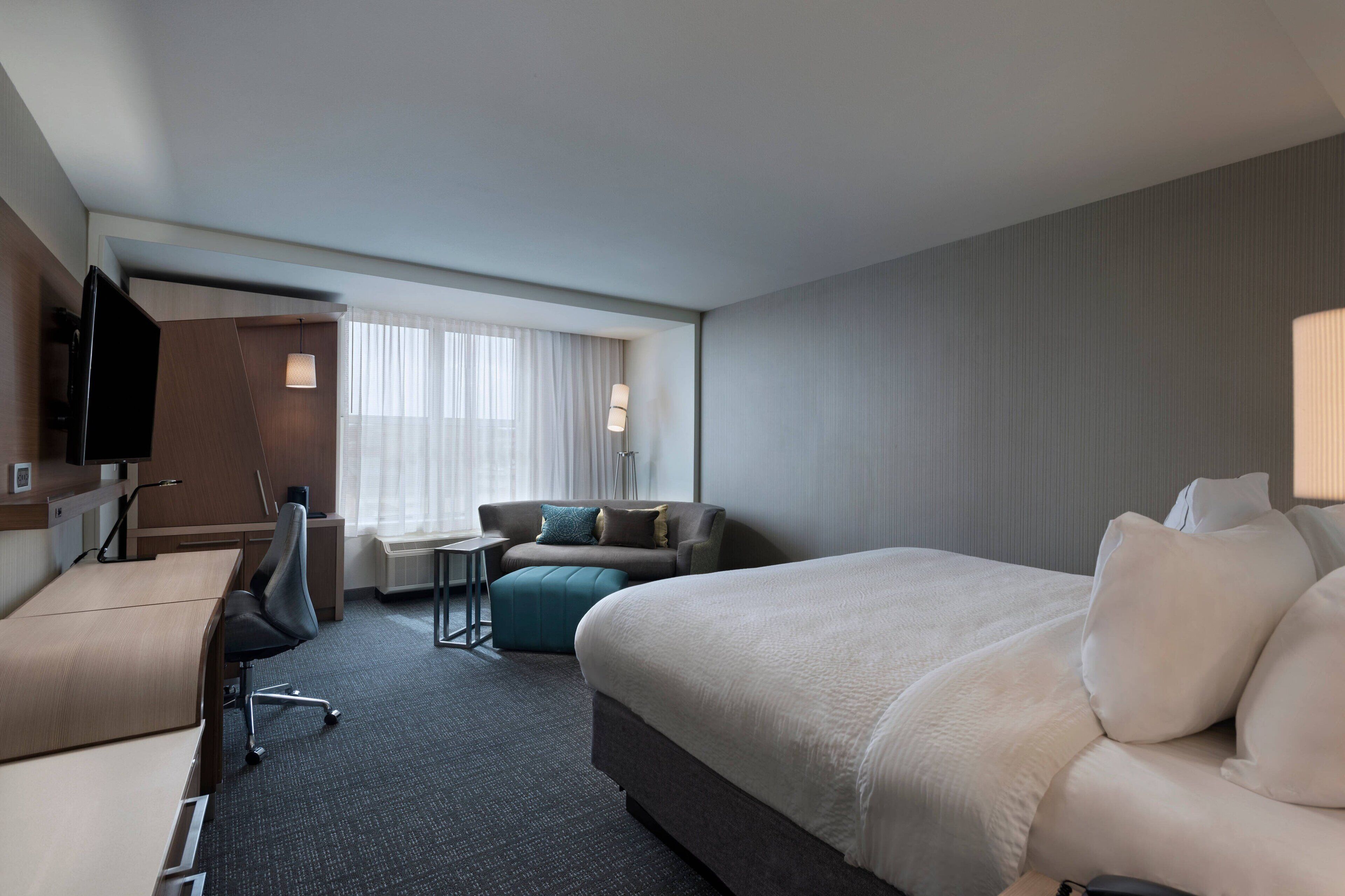 A hotel room with a bed, a desk, a chair, a TV, and a window with curtains.