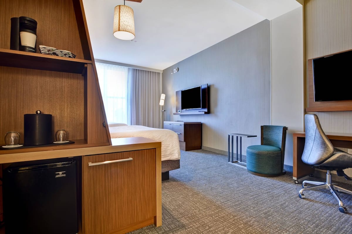 A hotel room with a bed, desk, chair, TV, and a small refrigerator.