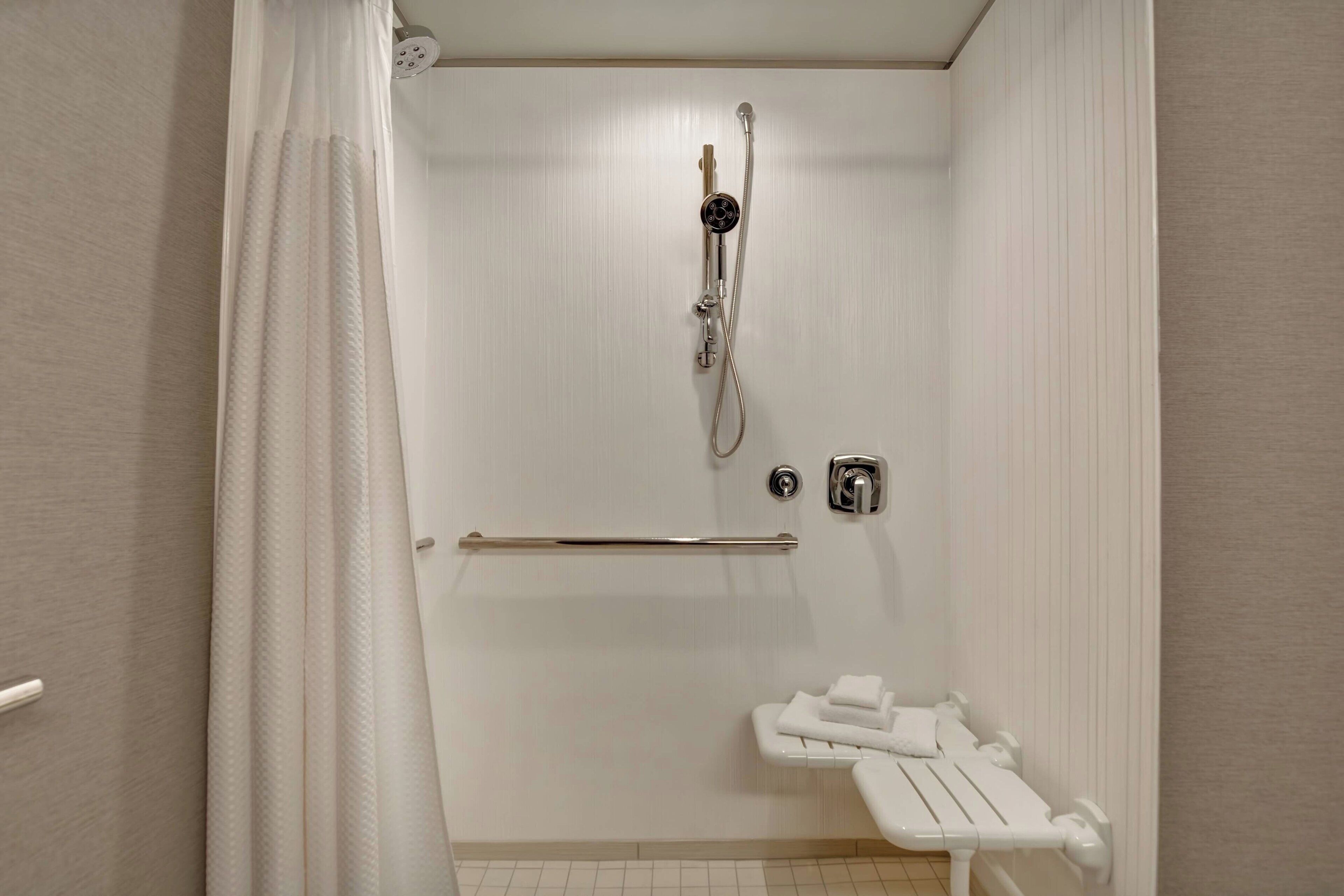 A small, white bathroom with a shower, a handrail, and a toilet.