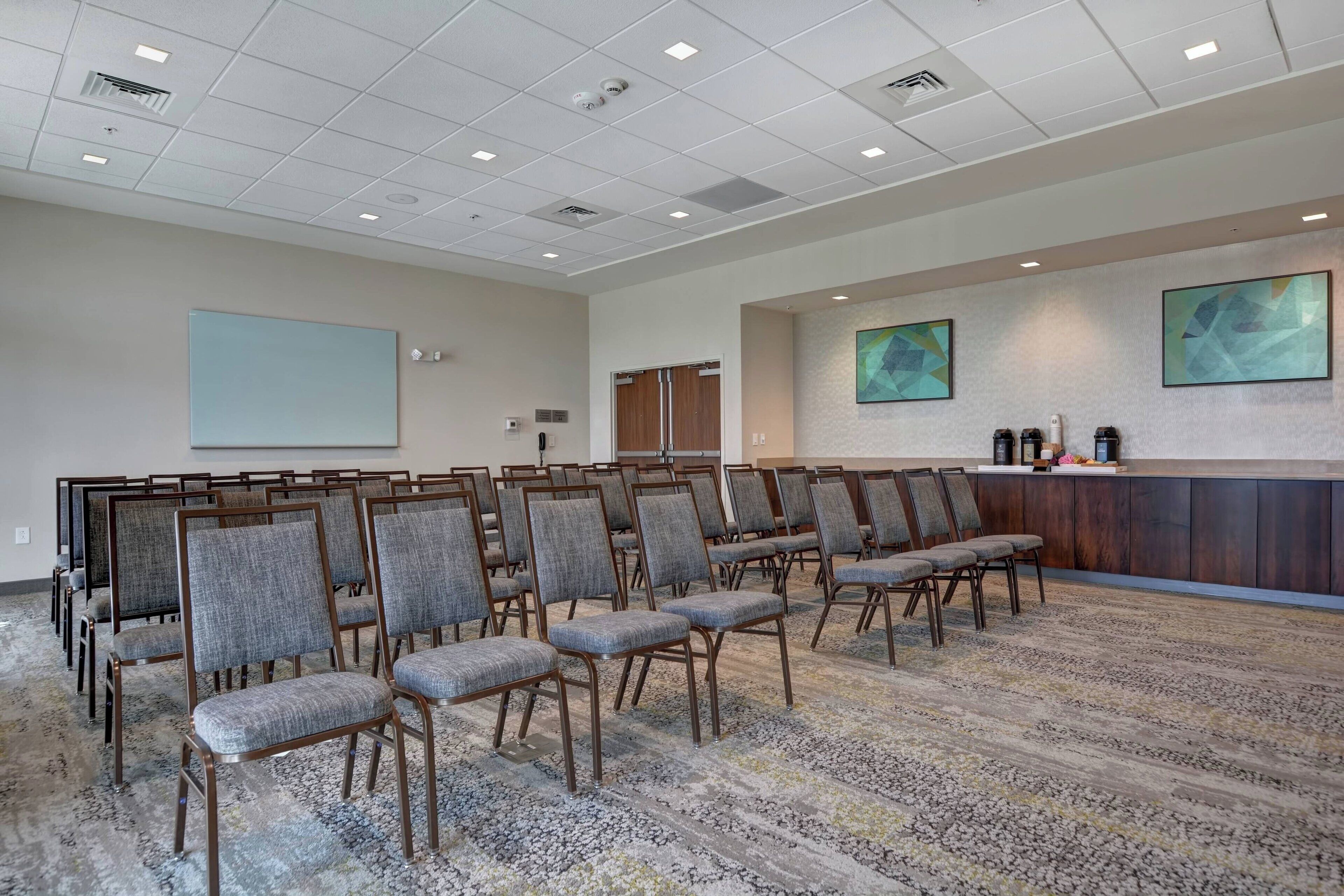 A conference room with rows of chairs, a projector screen, a reception desk, and abstract wall art.