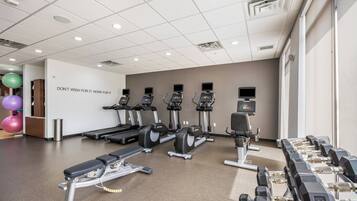 Une salle de sport équipée de tapis de course, de vélos elliptiques, d’un banc de musculation et d’haltères.