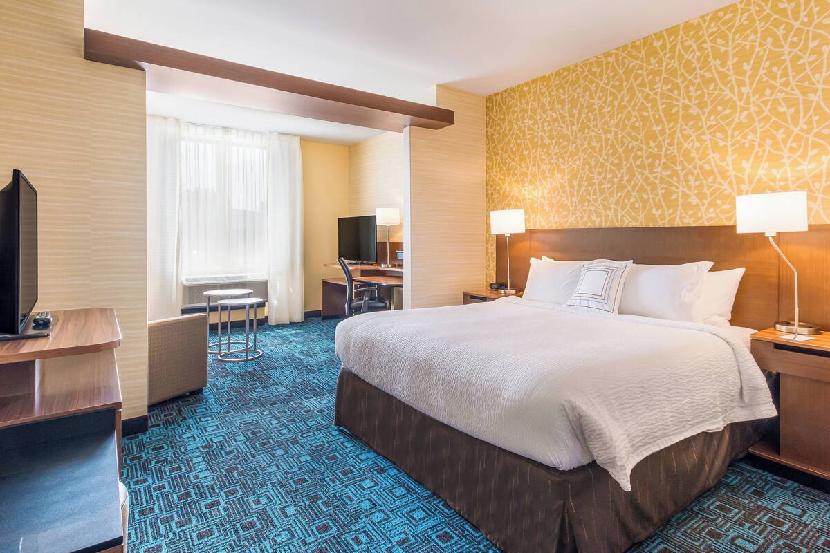 A hotel room with a large bed, a desk with a chair, a television, and a window with curtains.