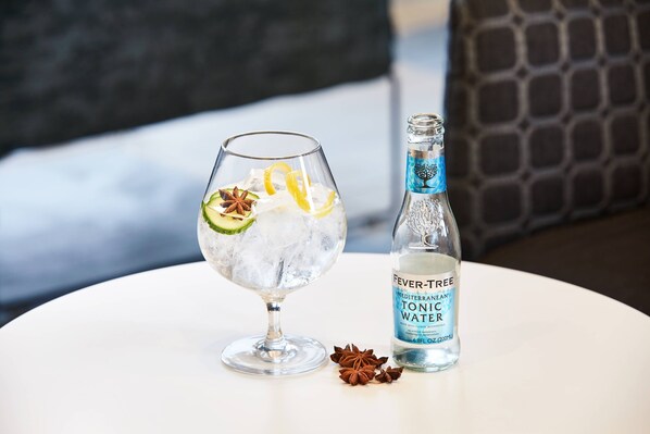 Un verre d’eau tonique glacée, agrémenté d’une tranche de citron et d’une étoile de badiane, posé sur une table blanche, à côté d’une bouteille d’eau tonique méditerranéenne de la marque Fever-Tree.