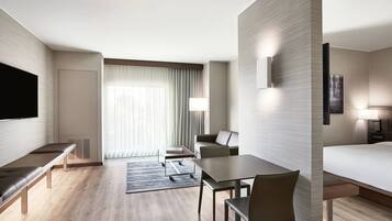 Une chambre d’hôtel moderne équipée d’un téléviseur à écran plat, d’un canapé, d’une table à manger avec des chaises, d’un lit et d’une grande fenêtre avec des rideaux.