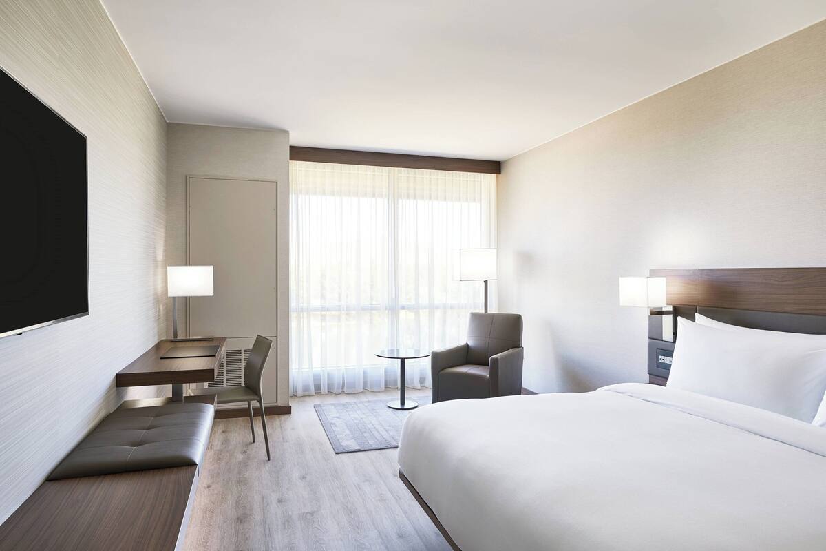 A modern hotel room with a large bed, a desk, a chair, and a TV.