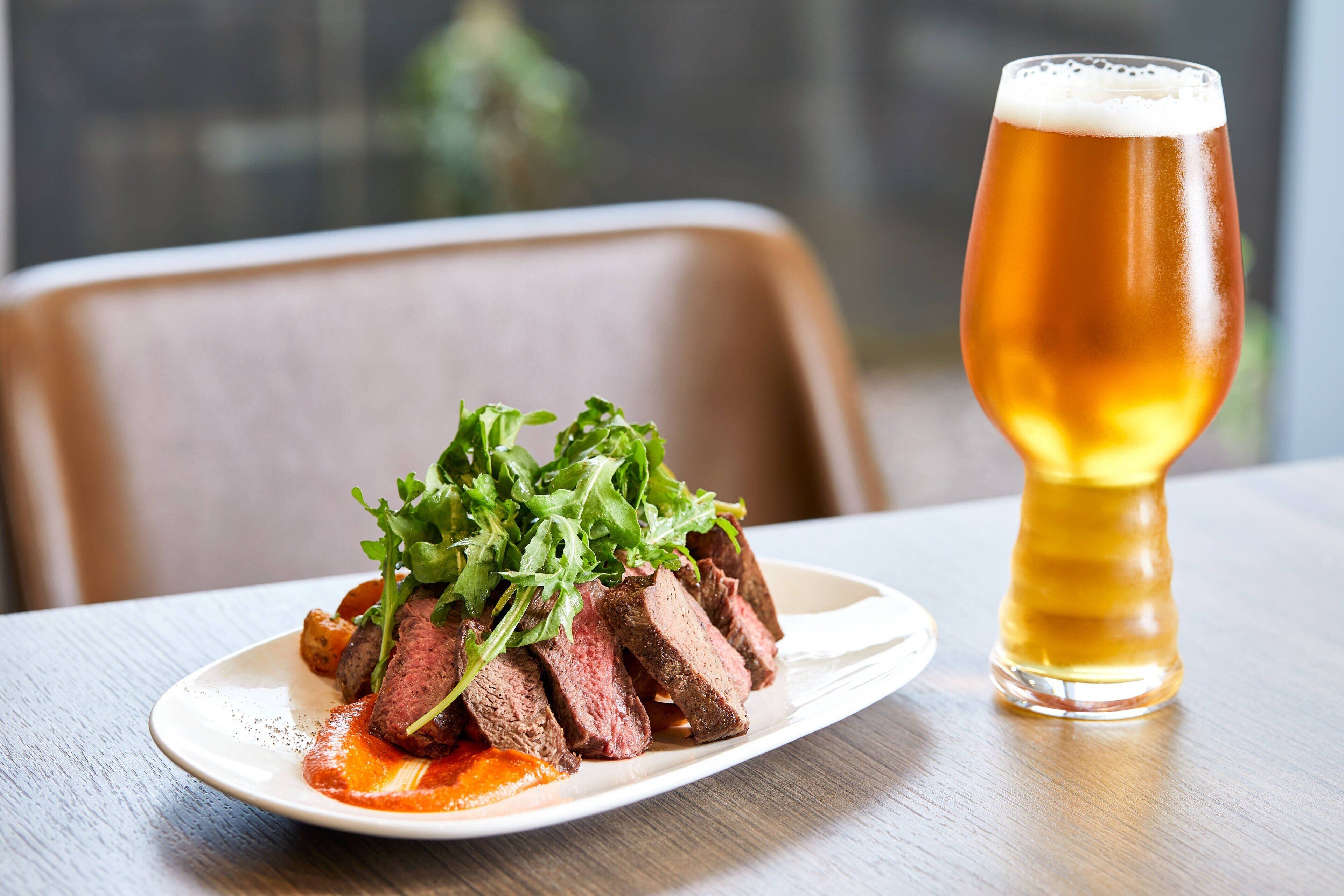 Un plato de carne con vegetales verdes y una jarra de cerveza sobre una mesa.