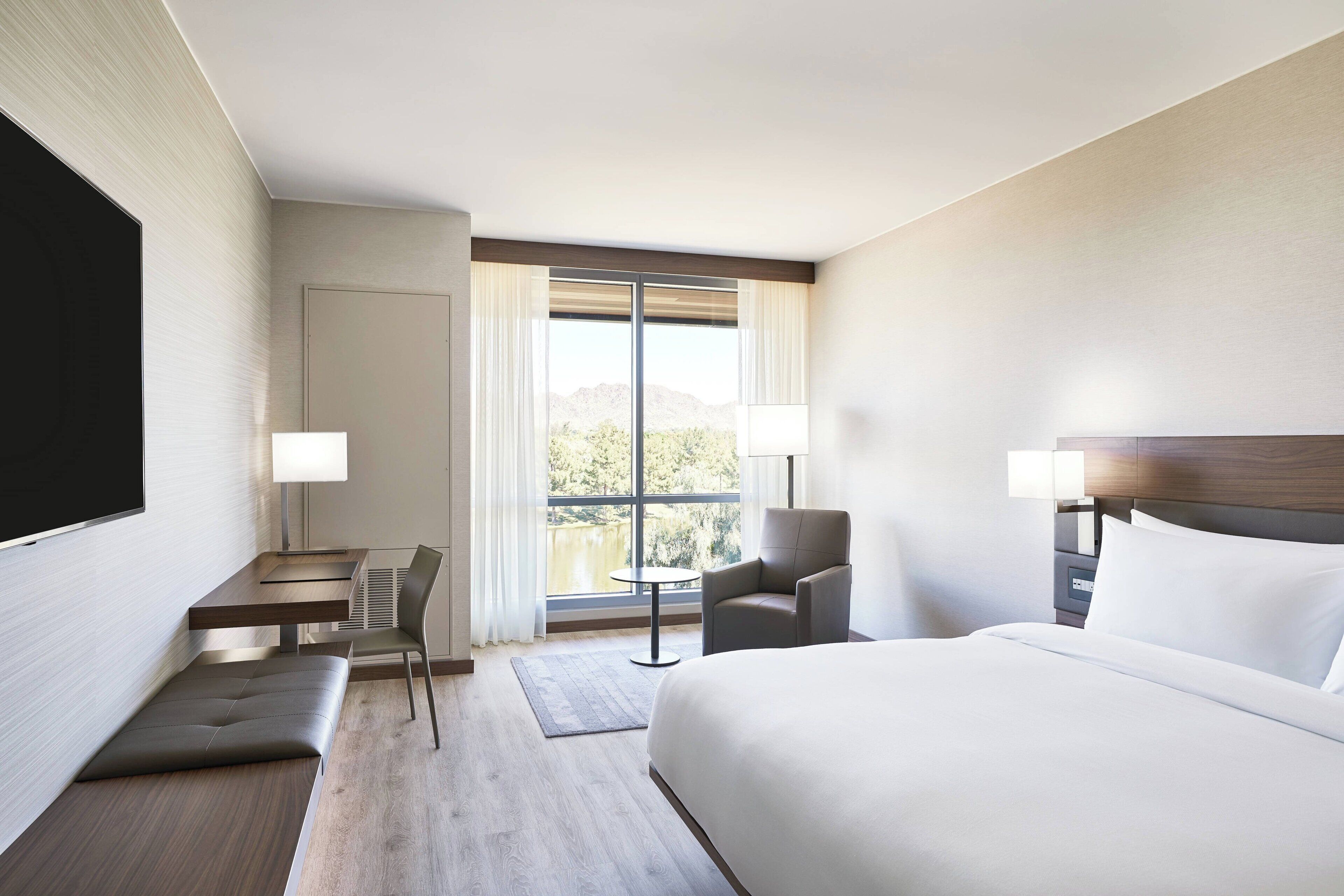 Quarto de hotel com uma cama, uma escrivaninha com cadeira, uma mesinha e vista para o exterior.