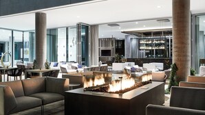 A modern lounge area with a central fire feature, comfortable seating, and a bar area in the background. - AC Hotel by Marriott Phoenix Biltmore (Phoenix)