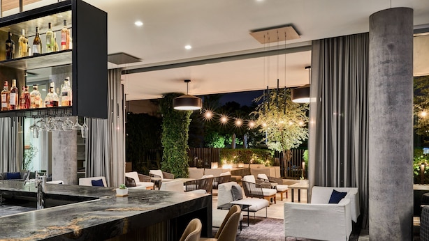 A modern bar area with a marble countertop, seating with white and brown chairs, and a variety of bottles on shelves. - AC Hotel by Marriott Phoenix Biltmore (Phoenix)