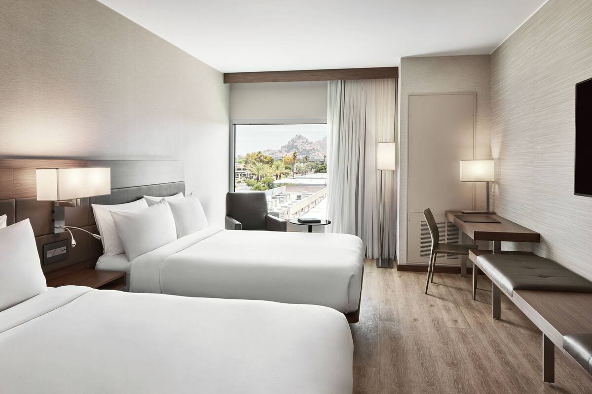 A hotel room with two beds, a desk, and a chair.