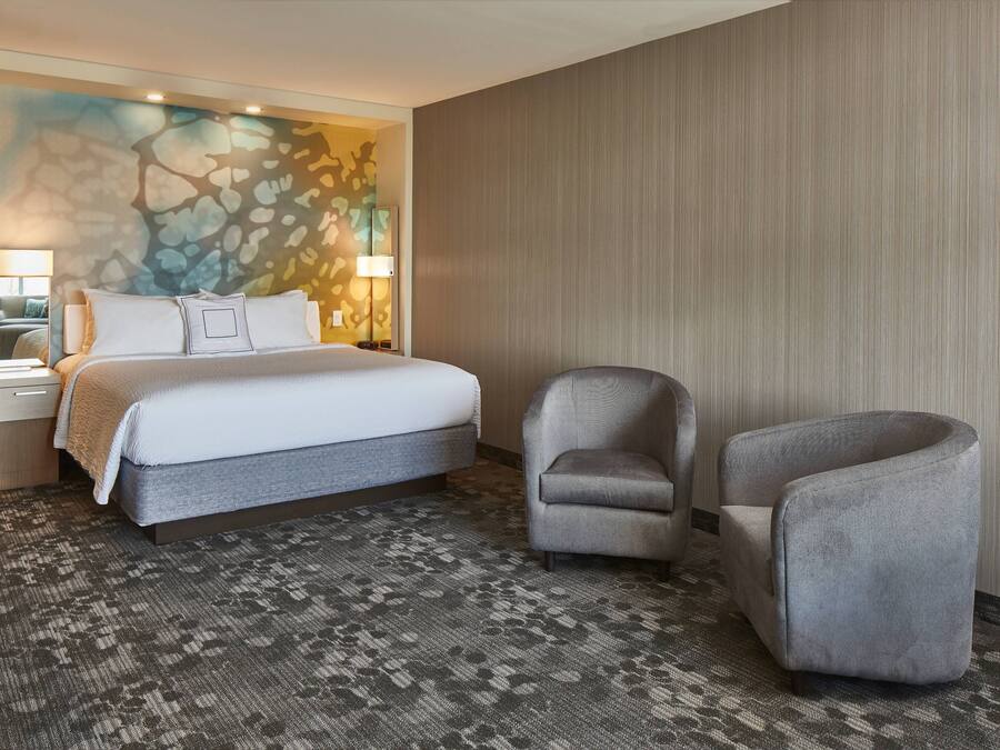 A hotel room with a large bed, two armchairs, a nightstand, a lamp, and a wall with a textured design.