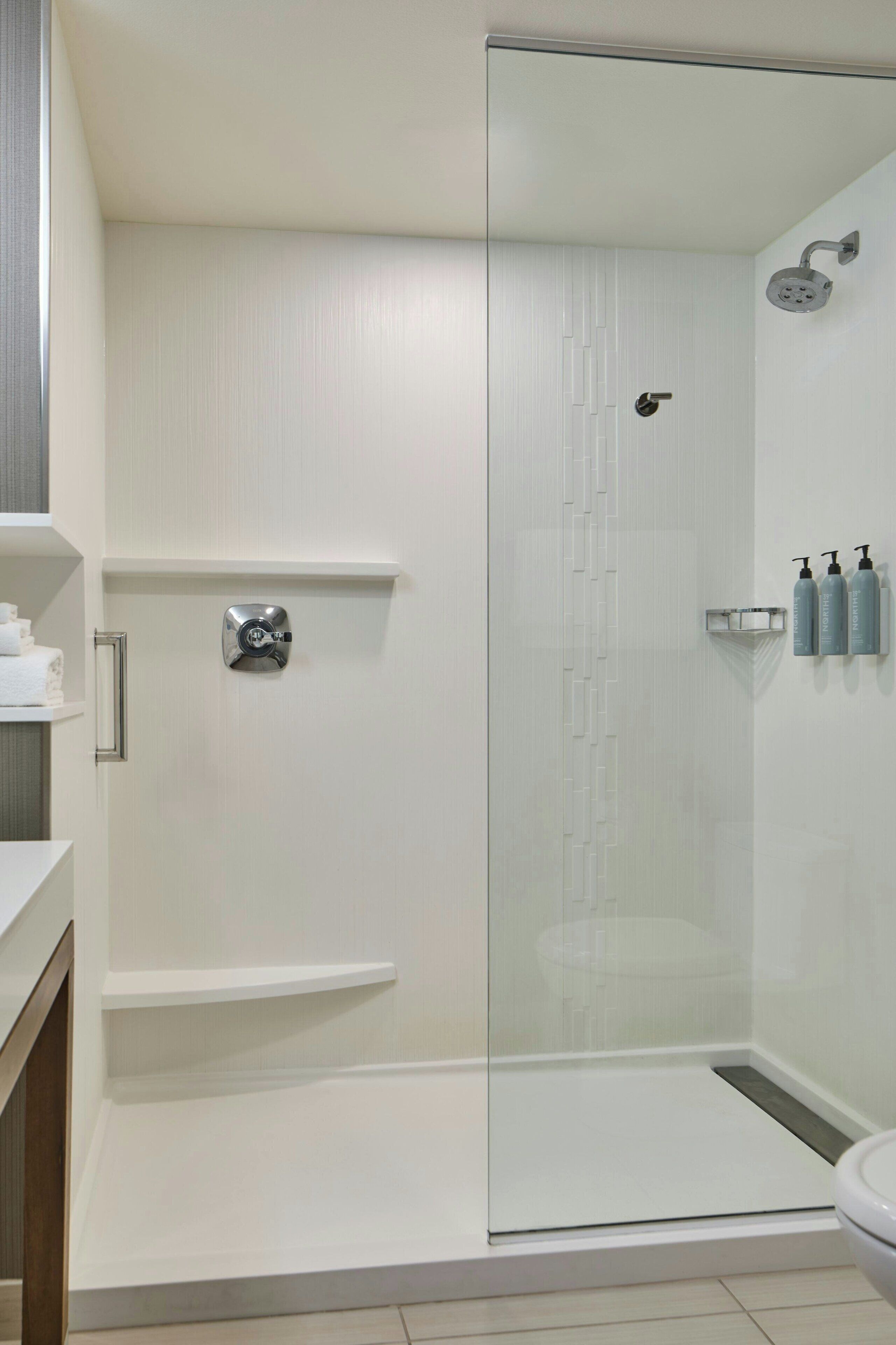 Un baño moderno con ducha envuelta en vidrio, inodoro y repisa con artículos de aseo.