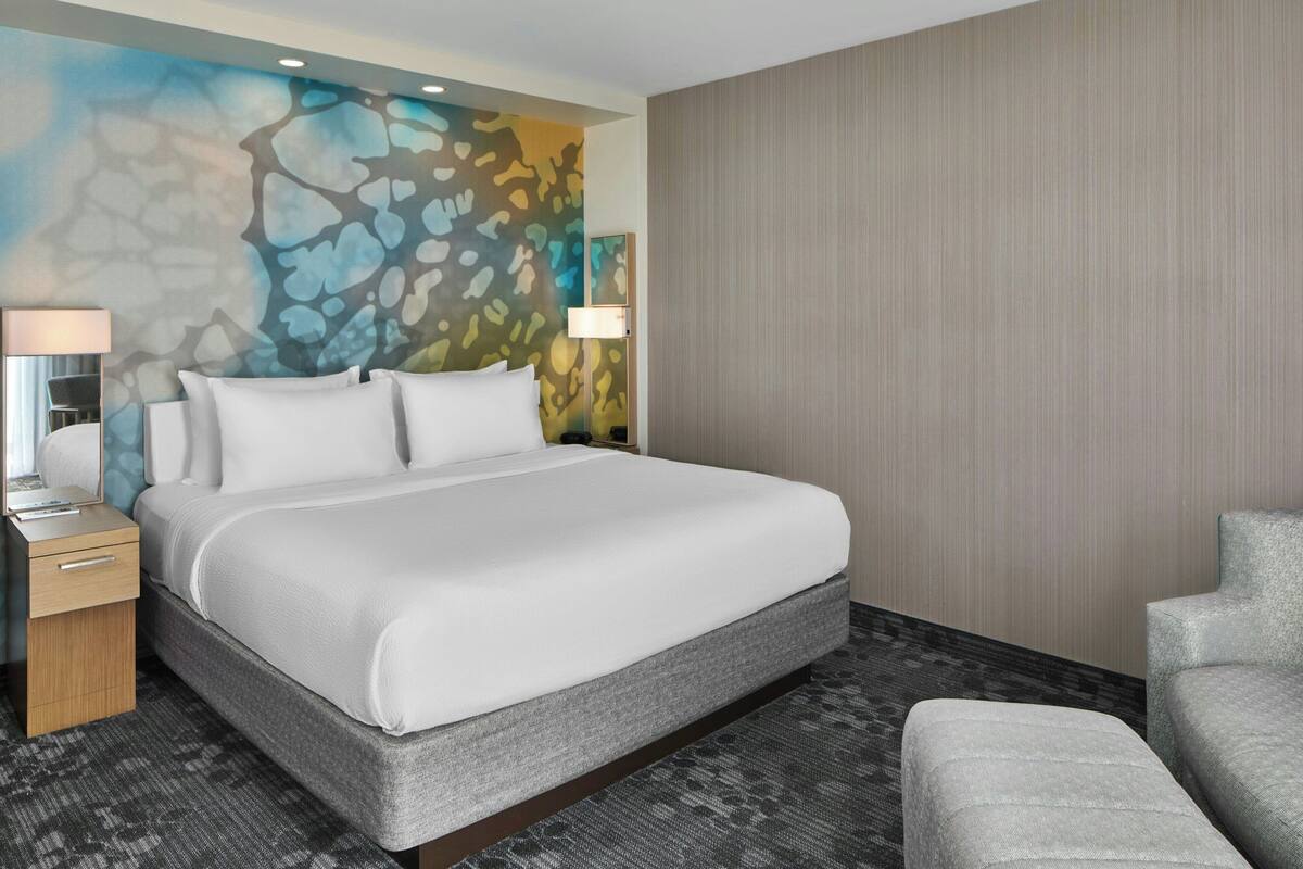 Ein Hotelzimmer mit einem gro ßen Bett, einem Nachttisch, einer Lampe und einem Sessel.