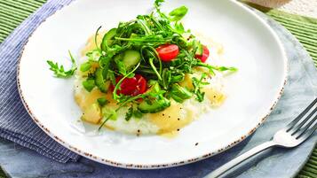 Een wit bord met een salade bovenop gepureerde aardappelen, op een blauw-witte geribbelde servet.