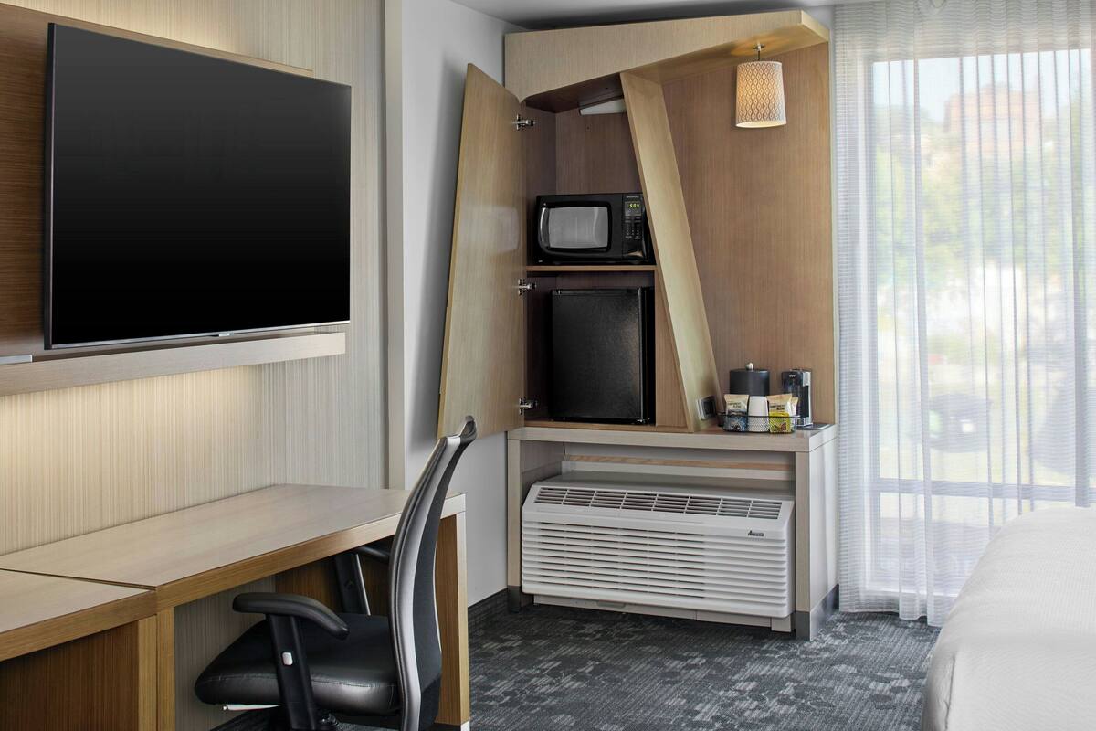 Ein Hotelzimmer mit Flachbildfernseher, Mikrowelle, Minikühlschrank, Schreibtisch mit Stuhl und einem Bett.