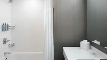 A modern bathroom with a bathtub, a shower, a vanity with a mirror, and toiletries.