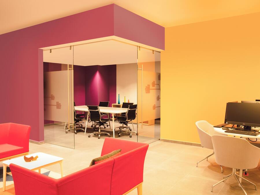 A modern office space with a meeting area, red and white furniture, and a computer setup.