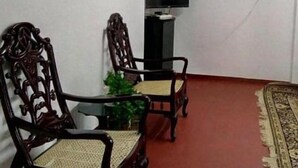 A room with two wooden chairs, a small table, a television on a stand, and a red carpet. - White Cottage Nuwara Eliya (Nuwara Eliya)
