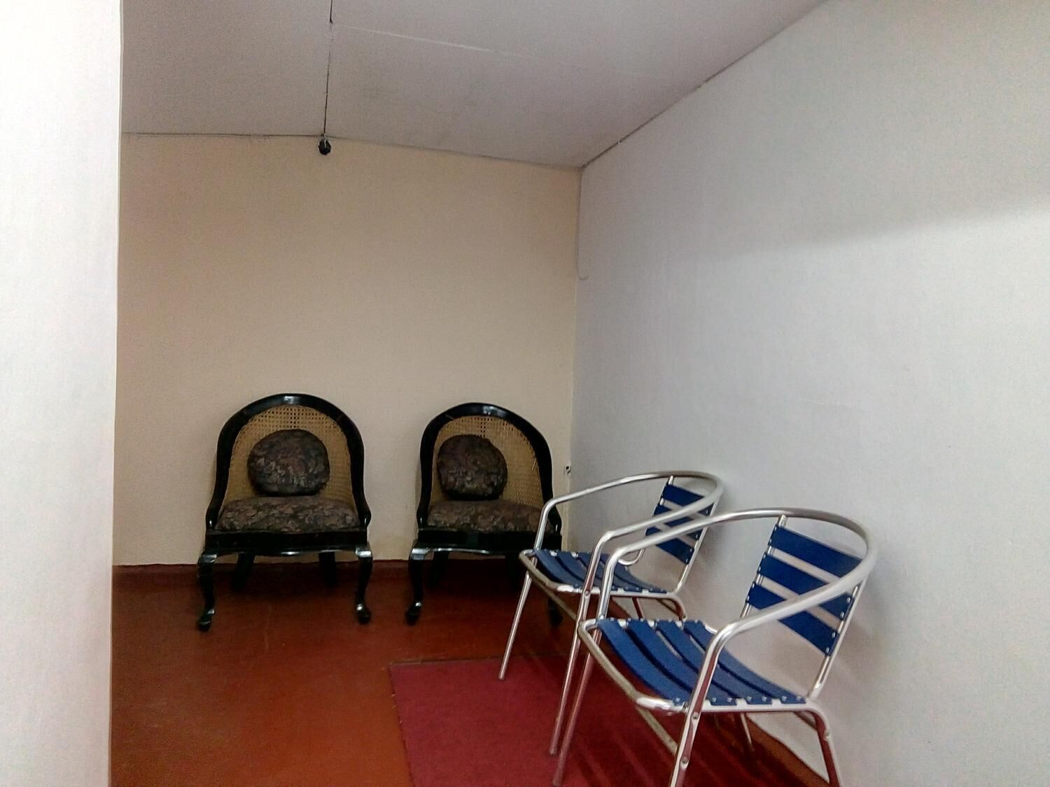 Ein Zimmer mit zwei hölzernen Stühlen mit gepolsterten Rückenlehnen sowie einem Stuhl aus Metall mit blau-weißen Streifen.