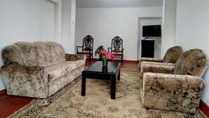 A living room with two sofas, a coffee table, and two armchairs. There is a television on the wall and a door in the background. - White Cottage Nuwara Eliya (Nuwara Eliya)