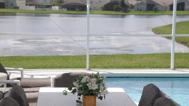 Un área junto a la piscina con una mesa, sillas, un florero y vista a un barrio residencial.