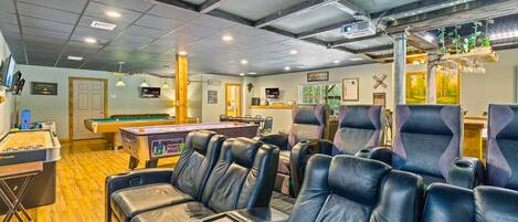 A billiards room with pool tables, comfortable seating, and a projector screen.