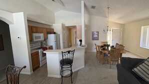 Una cocina moderna con armarios blancos, una isla central y un comedor con sillas y una mesa de madera.
