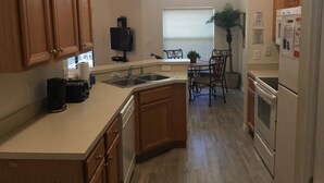 Una cocina con armarios de madera, horno empotrado, refrigerador, lavaplatos y un comedor con mesa y sillas.