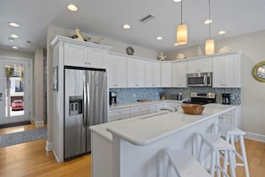 Une cuisine moderne avec des meubles blancs, des appareils en acier inoxydable, un grand îlot central et des luminaires suspendus.