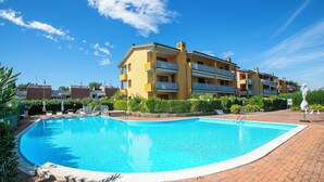 A swimming pool with a brick border, surrounded by a multi-story yellow building with balconies.