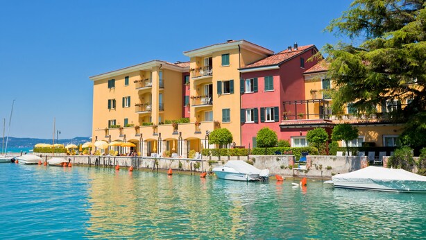 A waterfront hotel with multiple balconies, a marina with boats, and a clear blue sky.