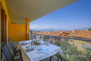 Een balkon met een eettafel, met uitzicht op een stadslandschap met rode daken en een heldere lucht.