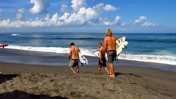 En strand med folk, der går og bærer surfboards.