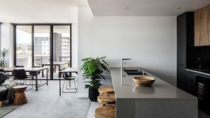 A modern kitchen with a large island, black cabinetry, and a view of the city. - Astra Apartments Wollongong (Wollongong)