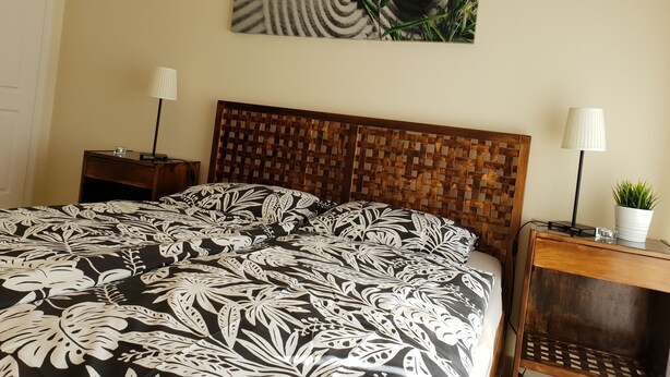 A bedroom with a bed, two bedside tables, a wall-mounted lamp, and a wall art piece.