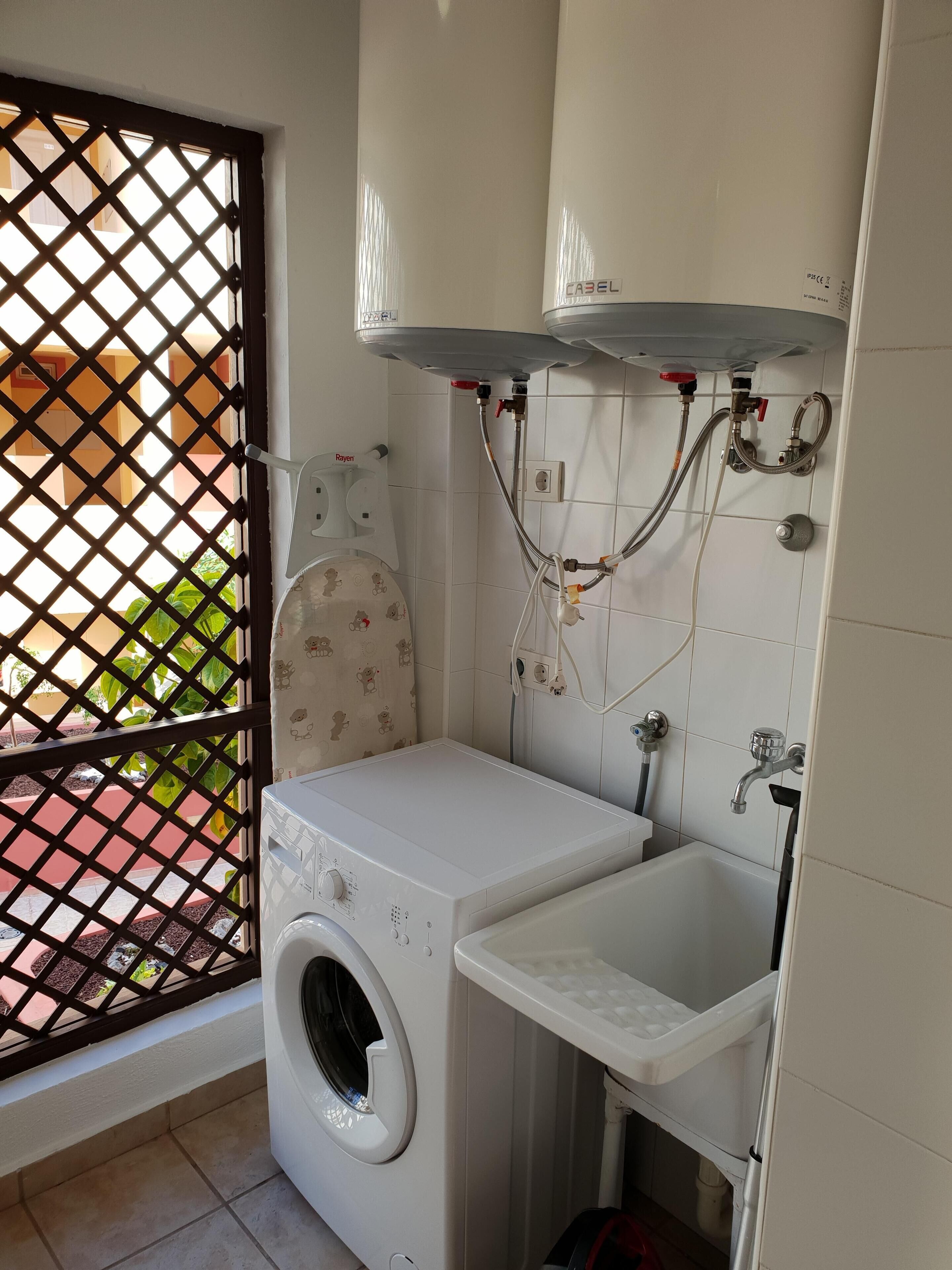 A compact laundry room with a washing machine, a sink, and a shower.