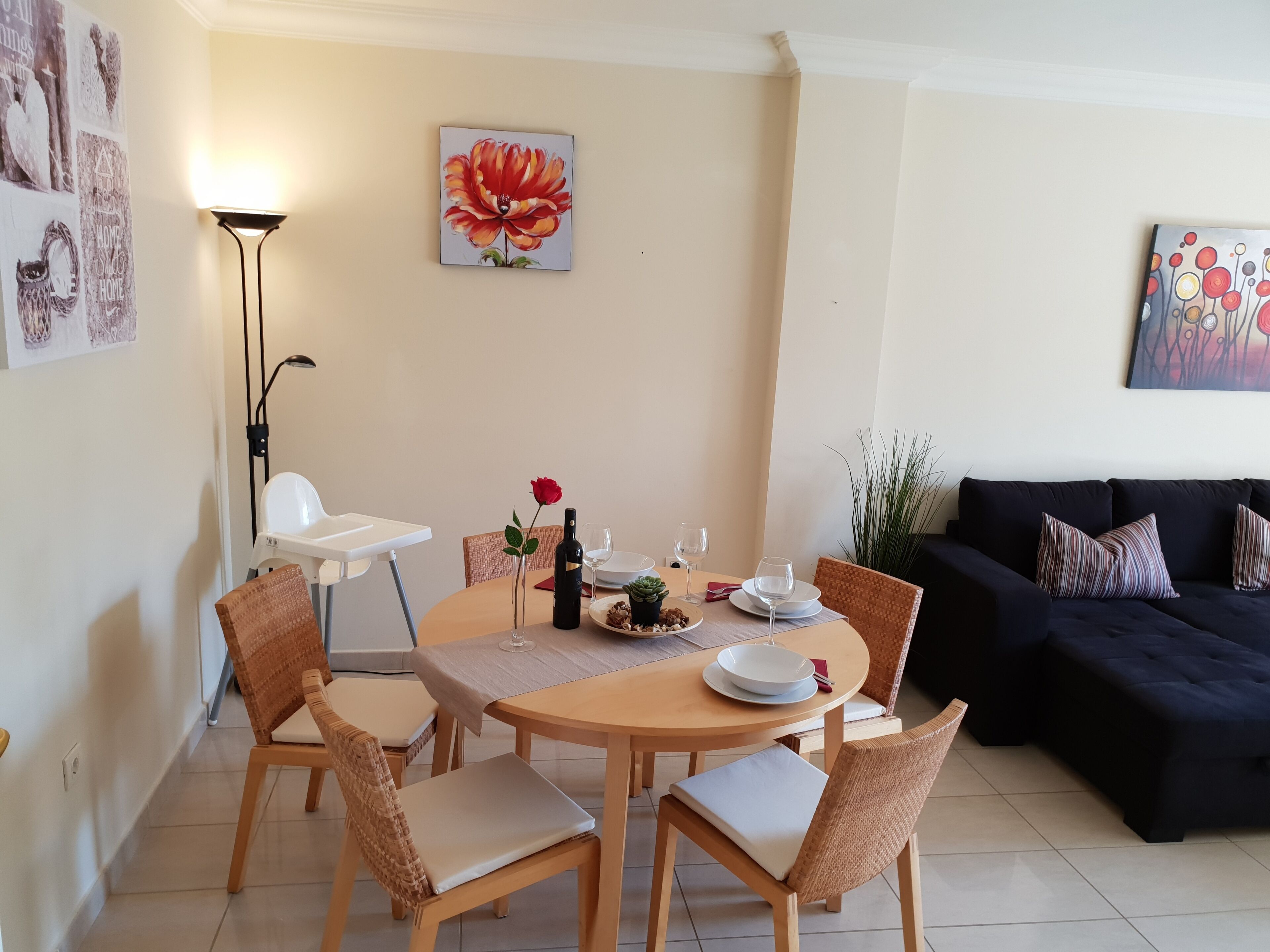 A dining area with a round table, four chairs, a bottle of wine, and a vase with a single red rose.
