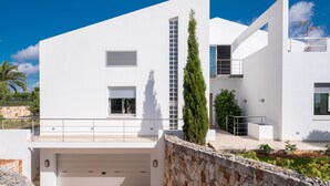 Un bâtiment moderne de couleur blanche, doté d’un garage, d’un mur en pierre et d’un grand arbre.
