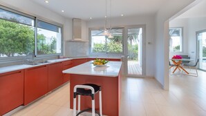 Une cuisine moderne dotée d’un grand îlot central, de meubles rouges et offrant une vue sur la verdure environnante.