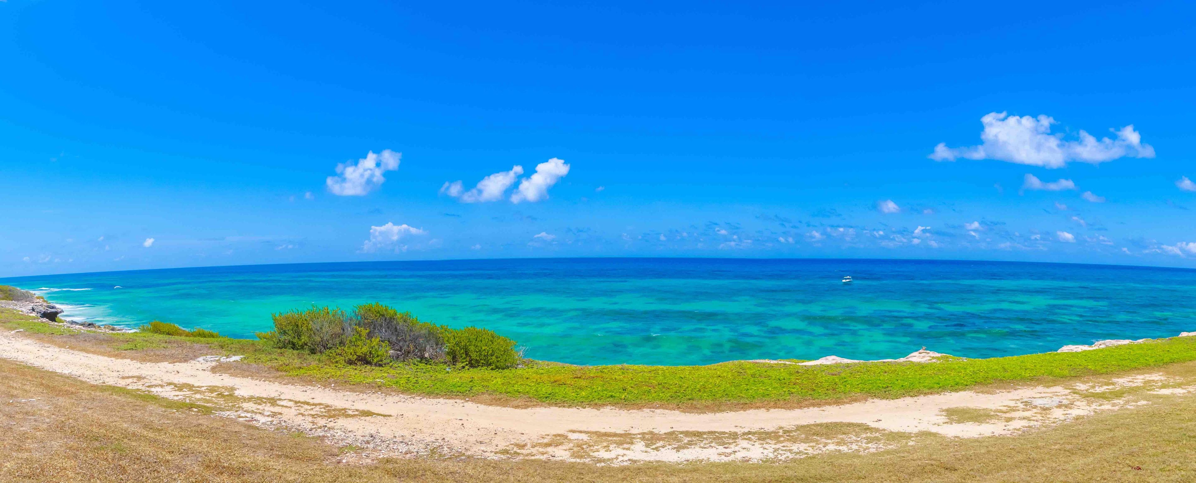 Eine Küstenlandschaft mit blauem Himmel, türkisblauem Meer und grüner Vegetation.