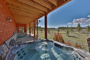 Un bain à remous sous une pergola en bois, avec vue sur un champ verdoyant et des arbres.