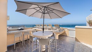 A terrace with a table and chairs, an umbrella, and a view of the sea.