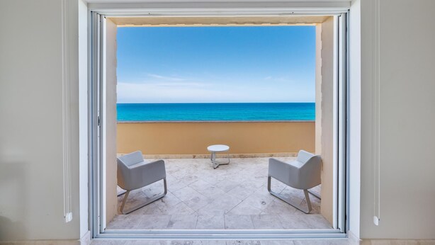 A balcony with a clear view of the sea, two chairs, and a small table.